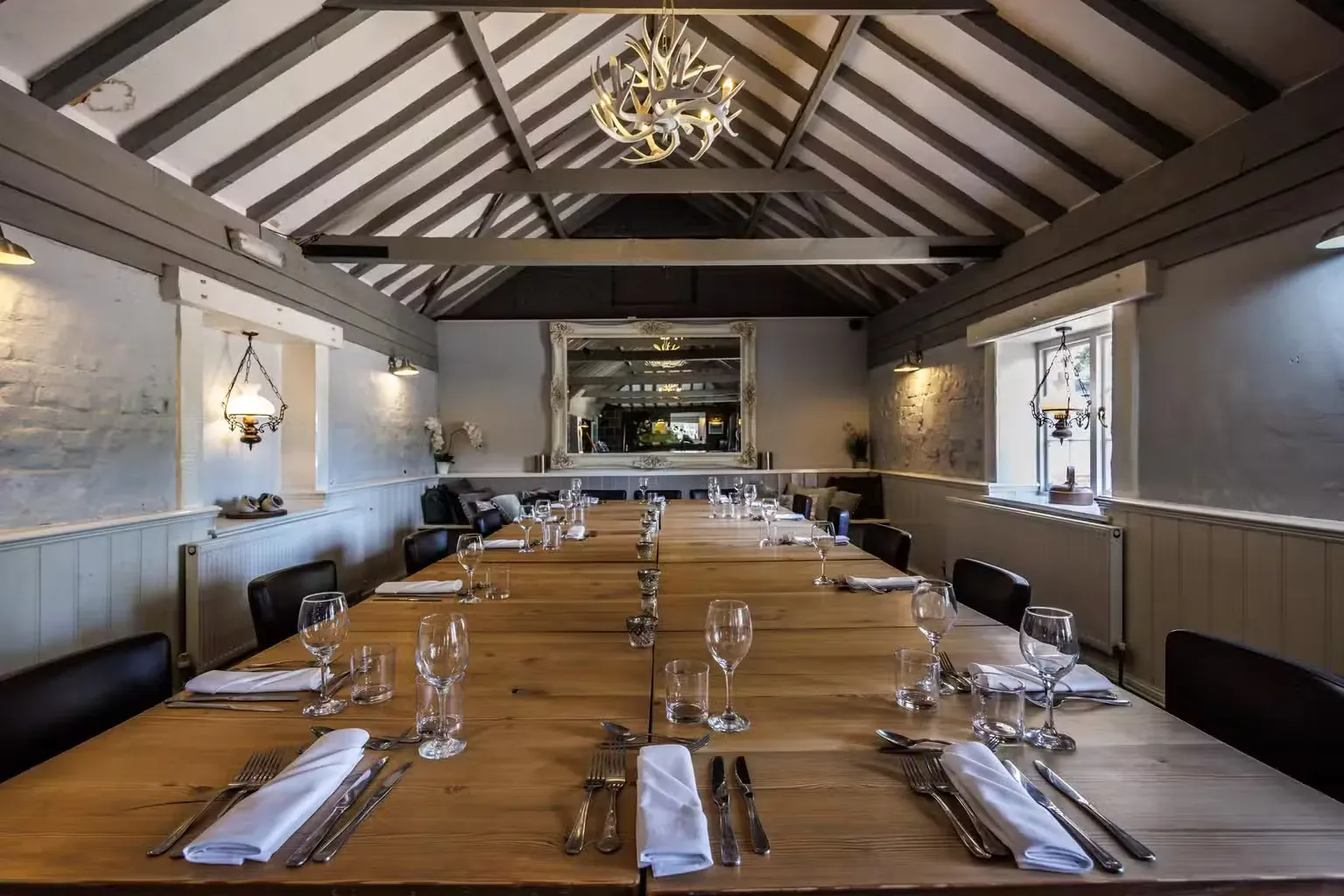 A long room under an open beamed roof, with one refectory table running its full length, laid with glasses and napkins.