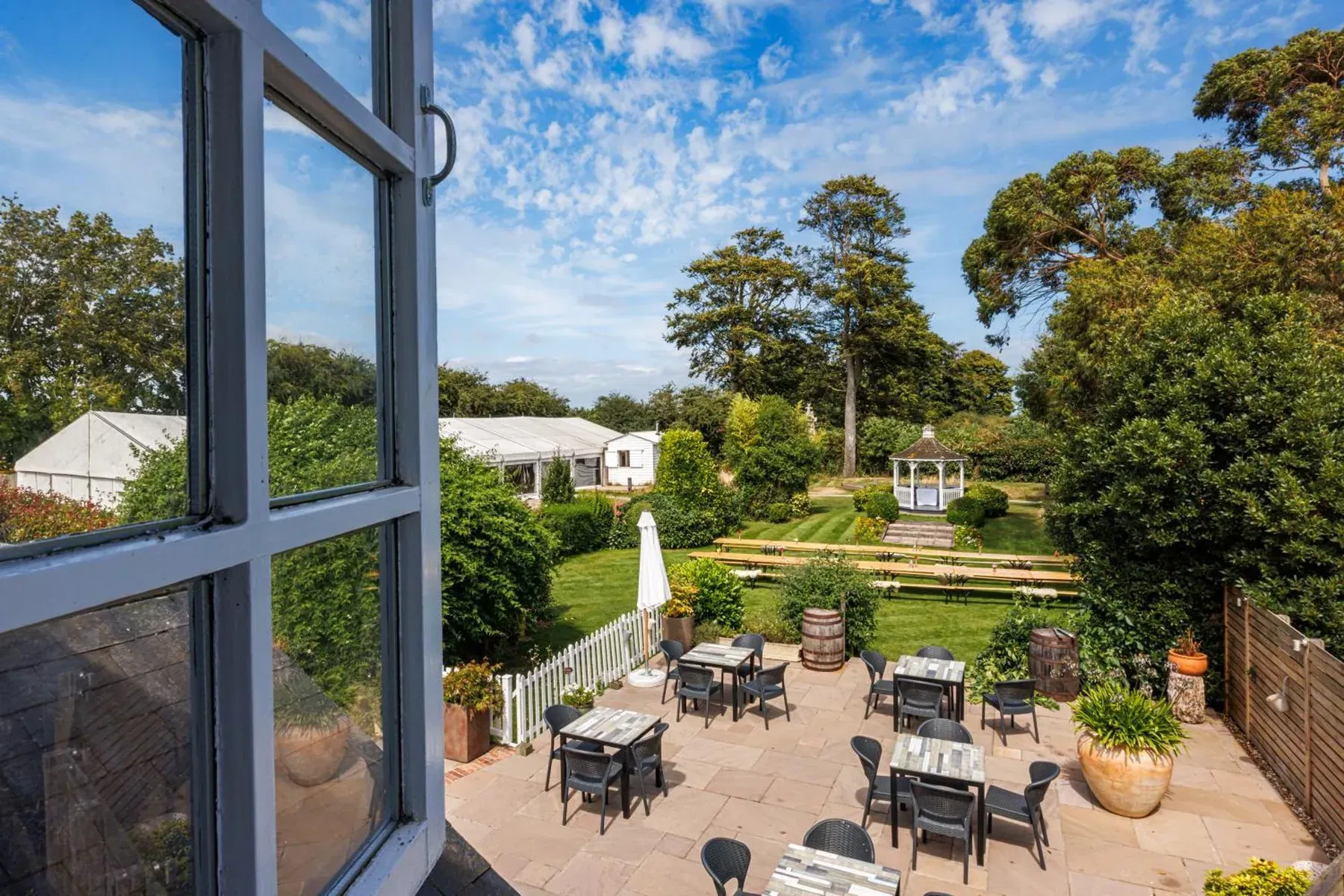 The terrace and lawn seen through a window, with a gazebo at the far end and a wide Kent sky above.